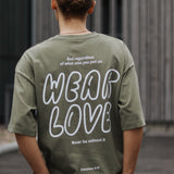 Person wearing a green t-shirt with 'Wear Love' text on the back, standing outdoors.
