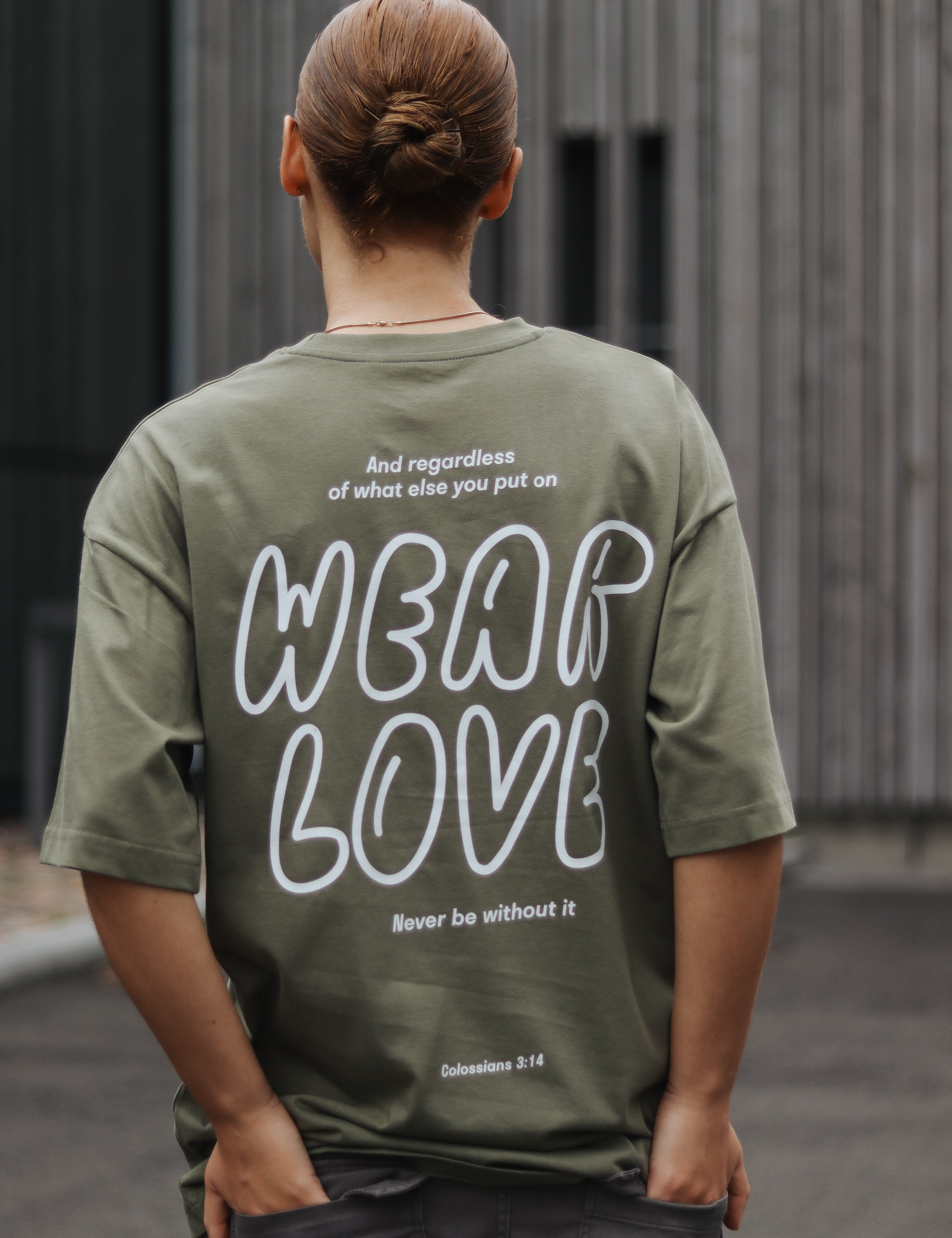 Person wearing a green t-shirt with 'Wear Love' text on the back, standing outdoors.