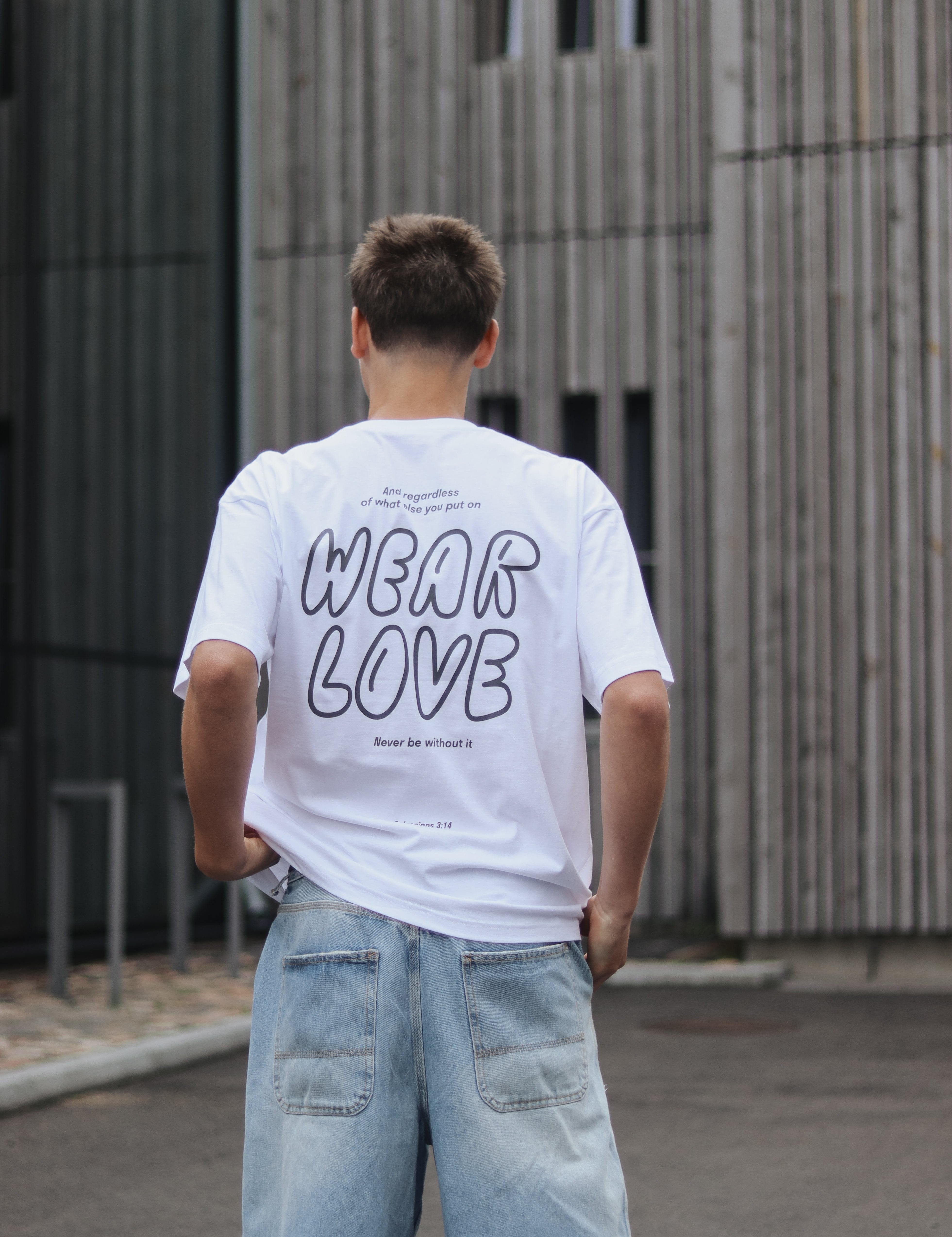 Person wearing a white t-shirt with 'WEAR LOVE' text, standing in front of a modern building.