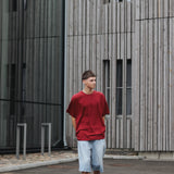 Person wearing a red shirt and light blue shorts standing in front of a modern building.