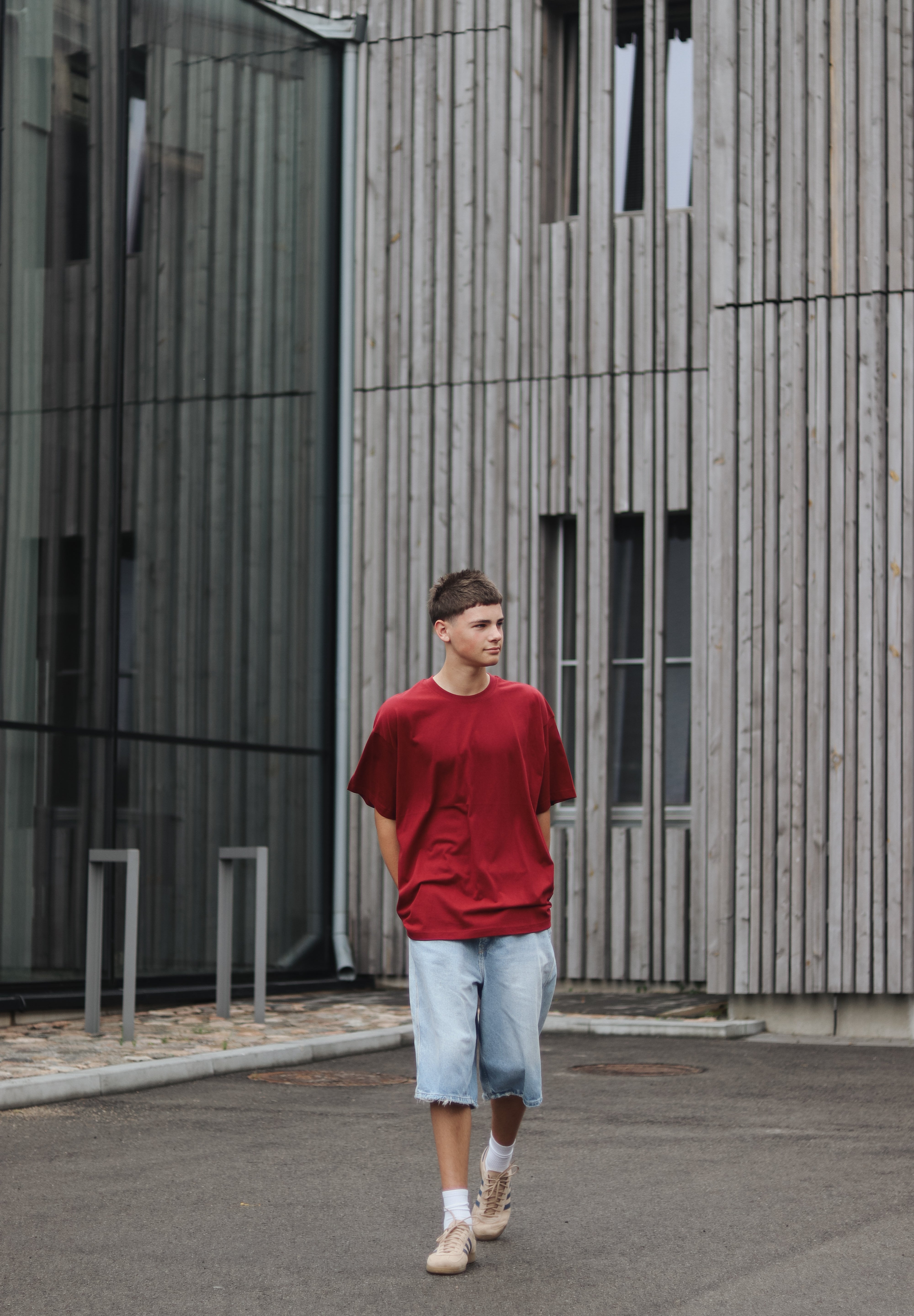 Person wearing a red shirt and light blue shorts standing in front of a modern building.