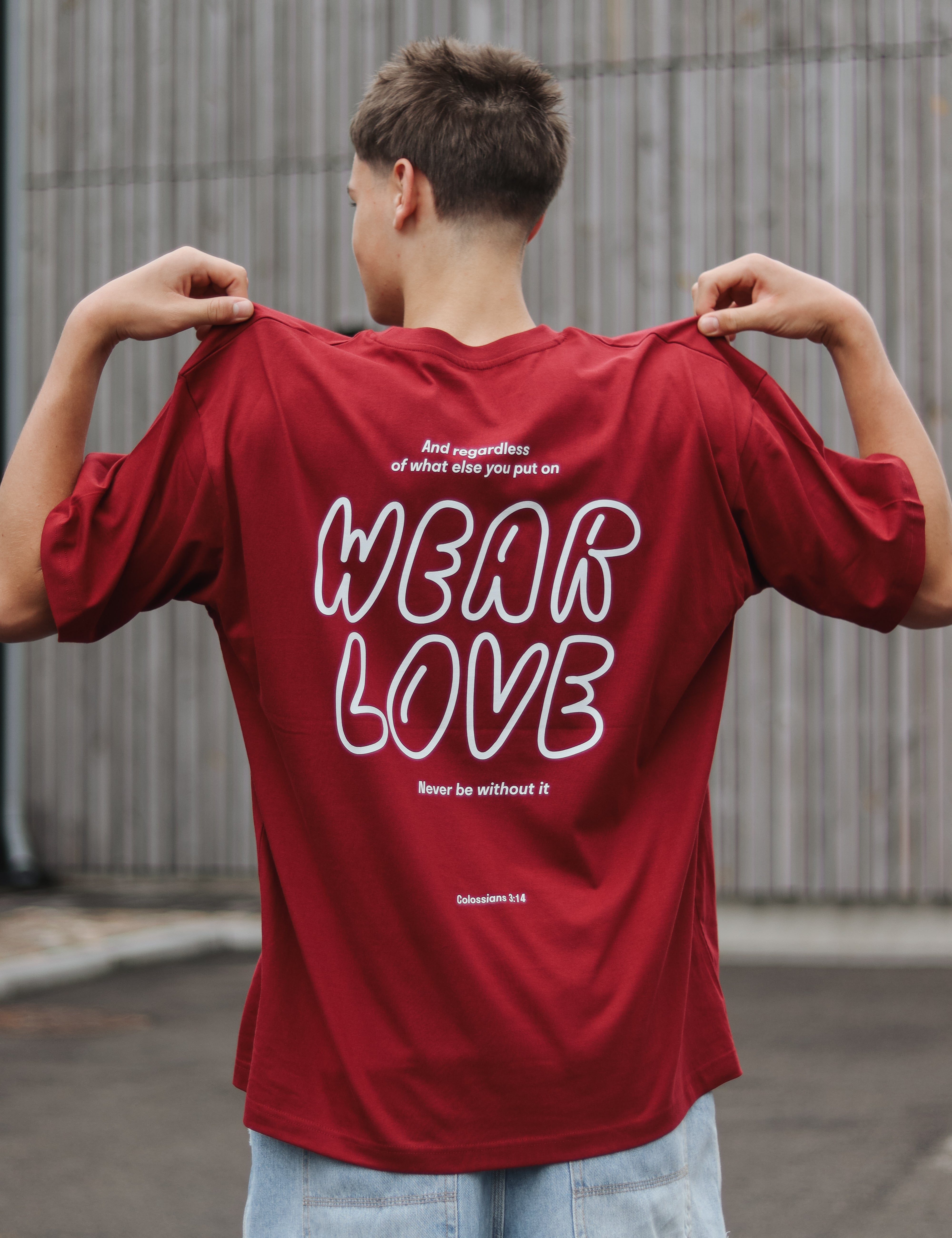 Person wearing a red t-shirt with 'WEAR LOVE' text on the back, standing outdoors.