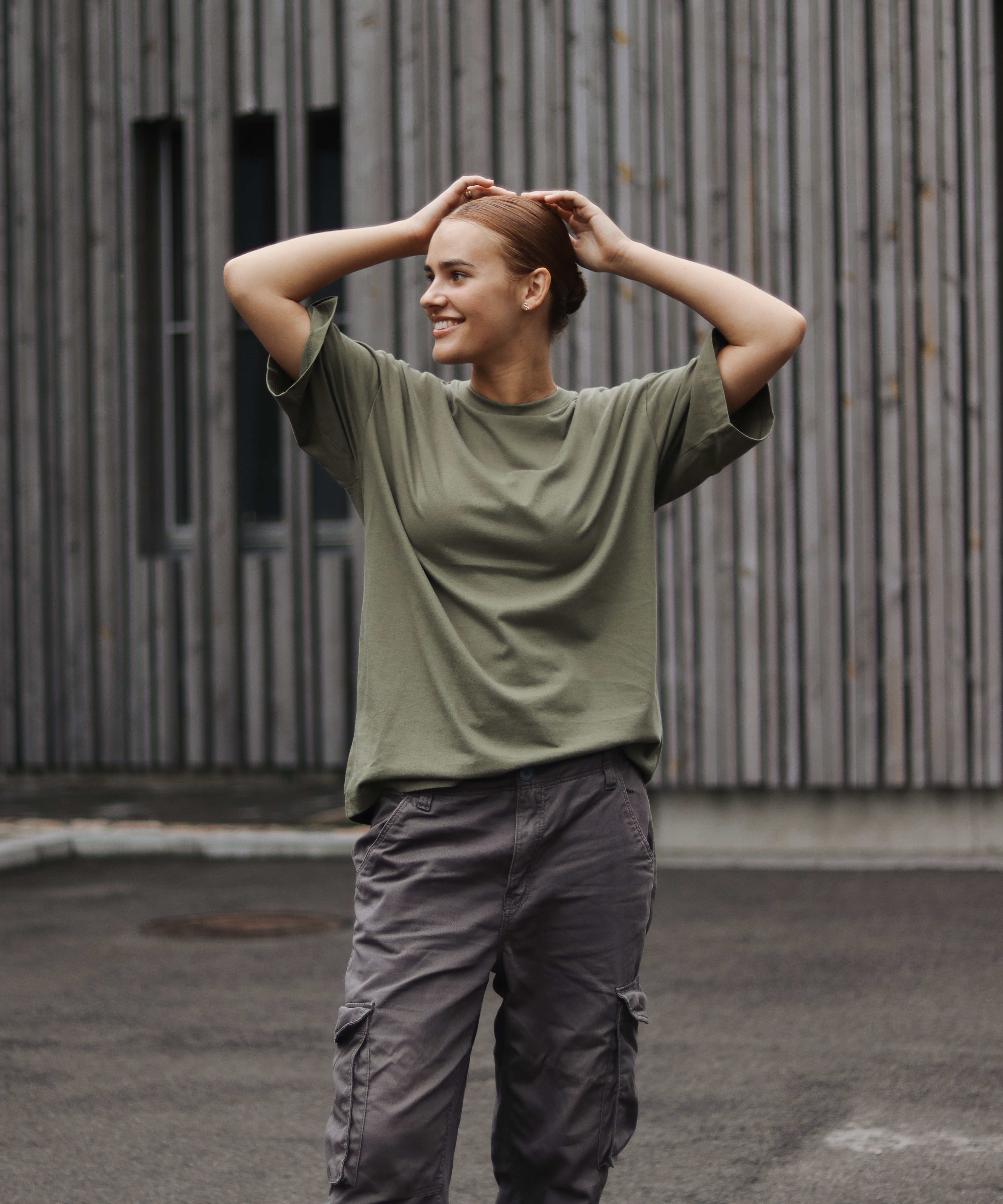 Person wearing a green shirt and gray pants standing outdoors against a wooden wall.
