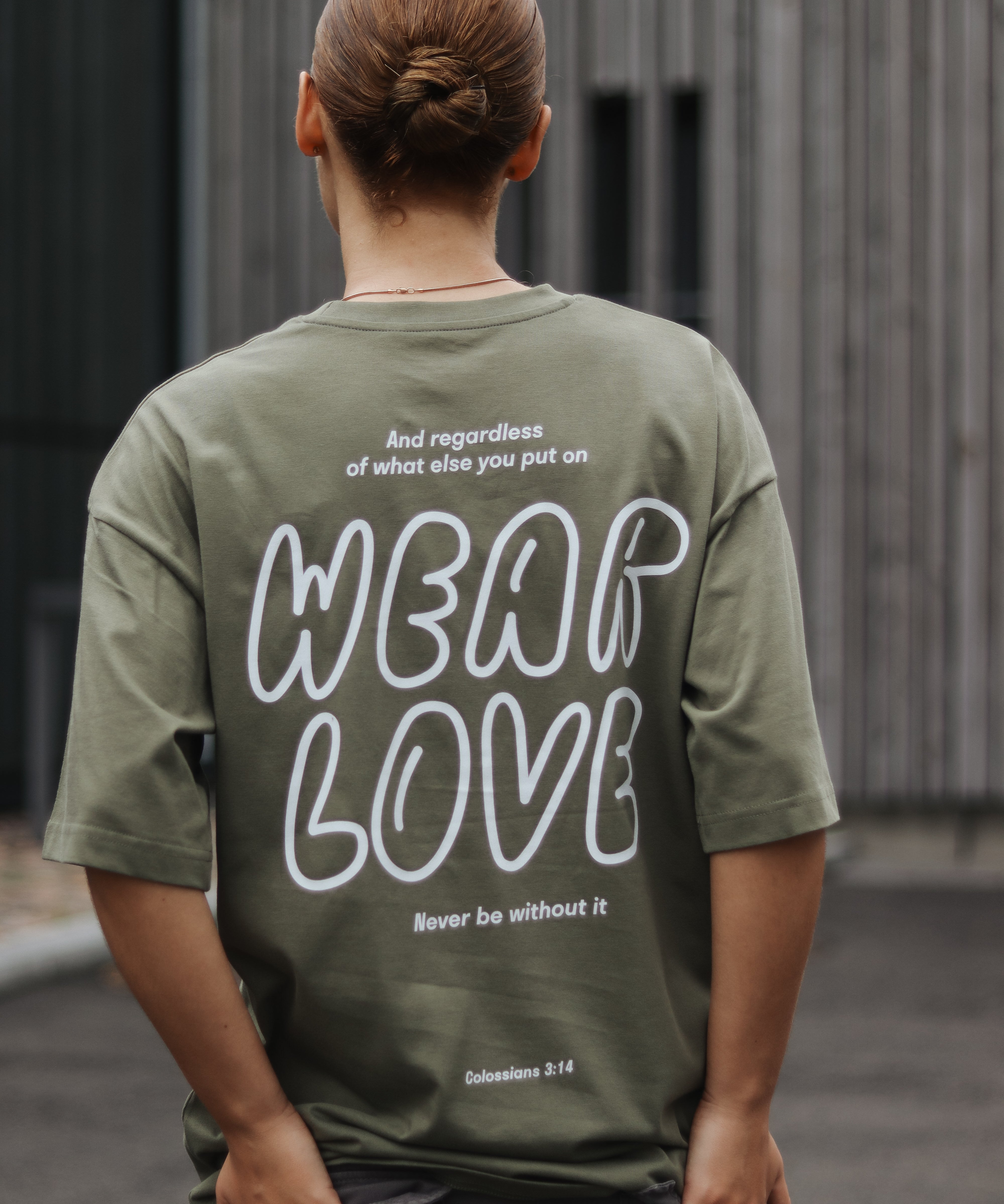 Person wearing a green t-shirt with 'Wear Love' text on the back, standing outdoors.