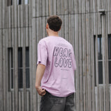 Person wearing a pink t-shirt with 'WEAR LOVE' text, standing in front of a wooden building.