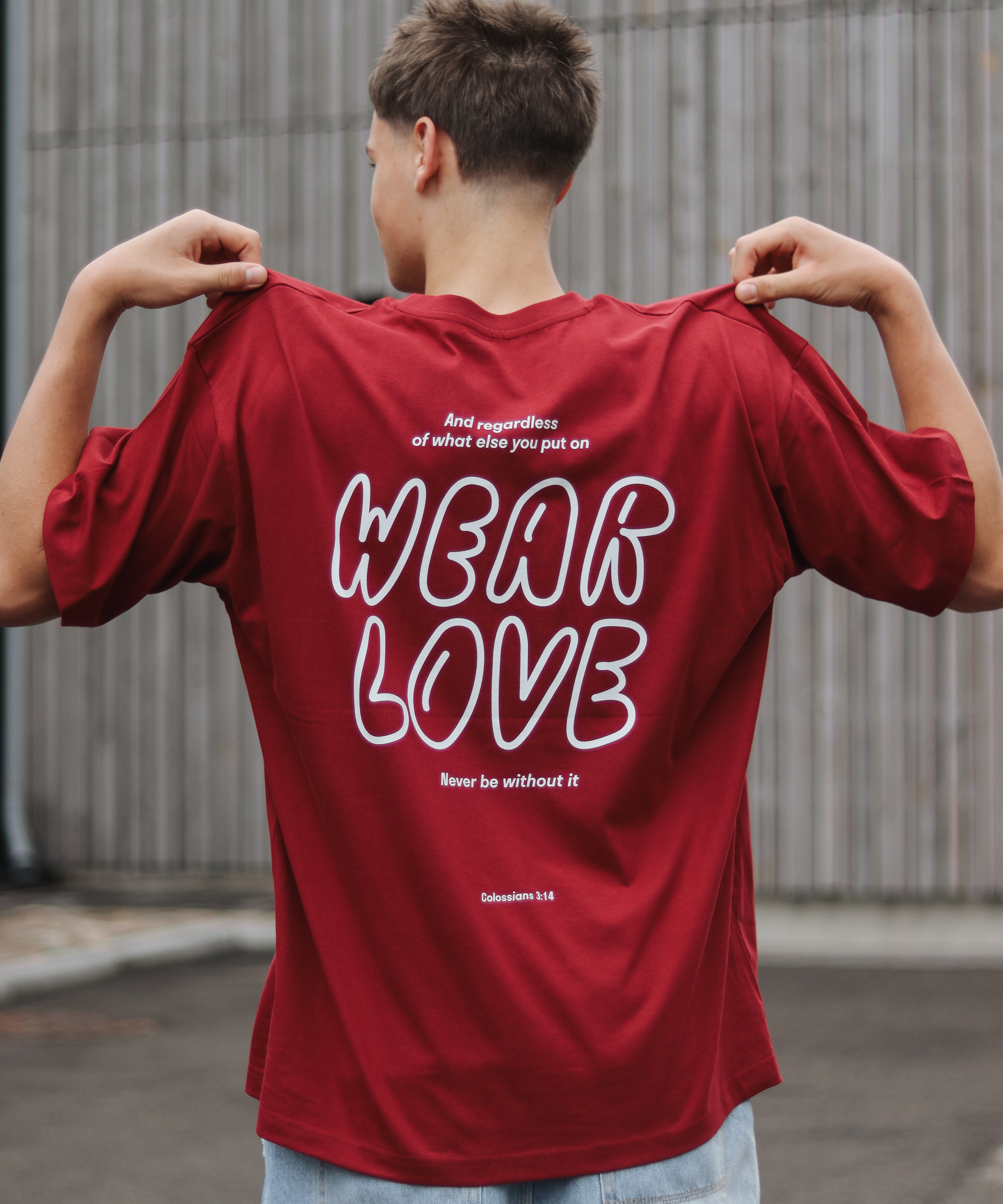 Person wearing a red t-shirt with 'WEAR LOVE' text on the back, standing outdoors.