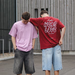 Two people standing outdoors, one wearing a pink t-shirt and the other a red t-shirt with 'Wear Love' text.