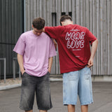 Two people standing outdoors, one wearing a pink t-shirt and the other a red t-shirt with 'Wear Love' text.
