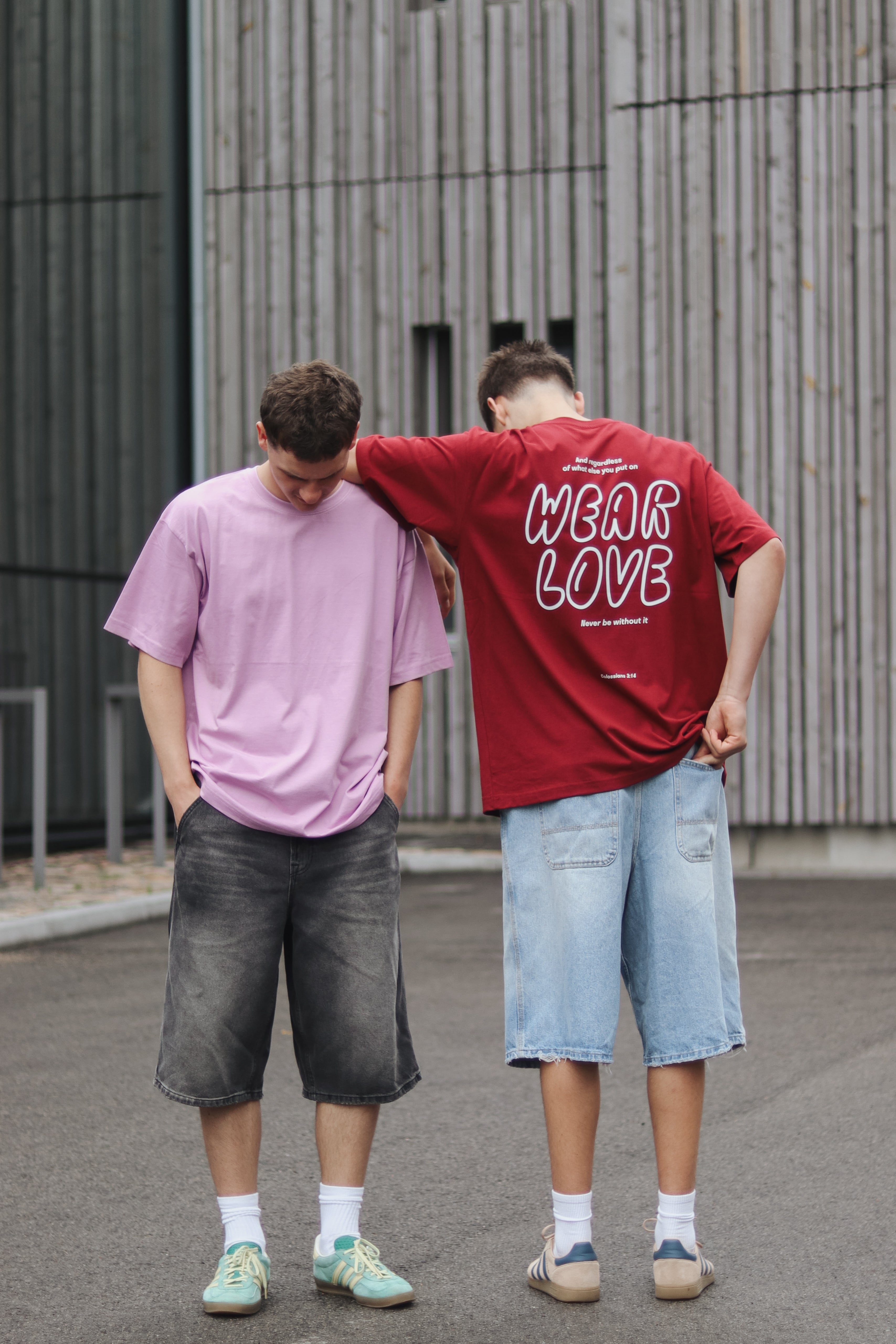 Two people standing outdoors, one wearing a pink t-shirt and the other a red t-shirt with 'Wear Love' text.
